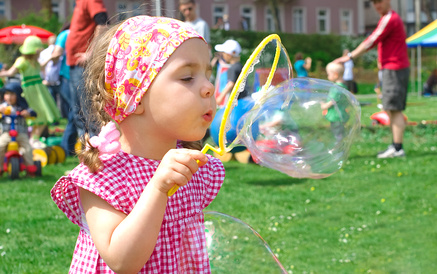 Bild Mädchen blässt eine Seifenblase auf einem Spielplatz, Kinder im Hintergrund