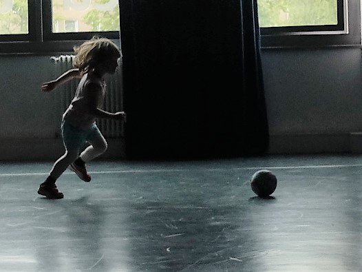 Foto: kleines Mädchen in einer Turnhalle rennt einem Ball hinterher