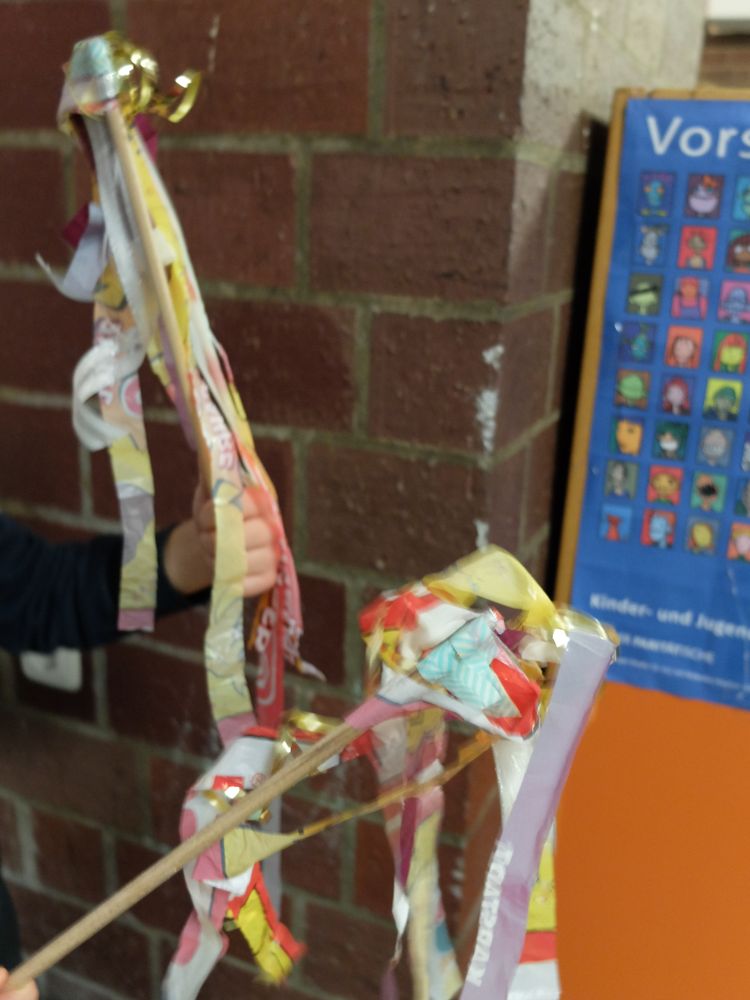 Foto: Kinderhände halten slebsgebaute Fahnen aus bunten Plastikstreifen an Holzstäben
