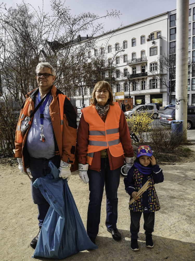 Foto: 2 Erwachsene in Warnwesten mit Müllbeutel und ein Kind stehen nebeneinander mit Blick zum Betrachter