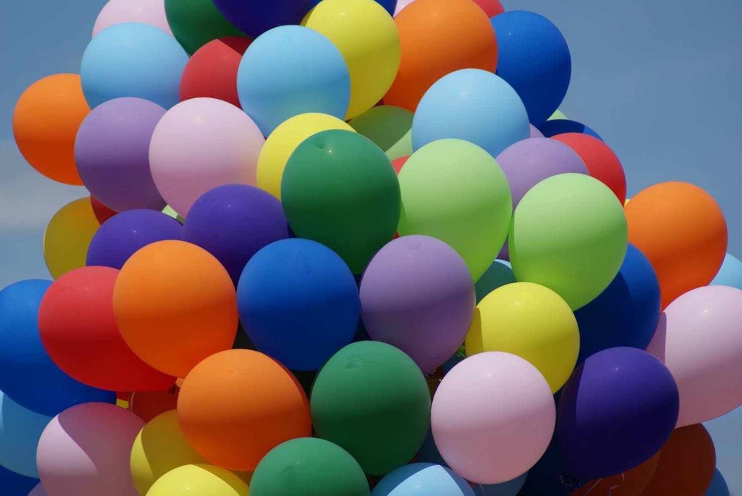 Foto: eine große Traube bestehend aus vielen bunte Luftballons vor blauem Himmel