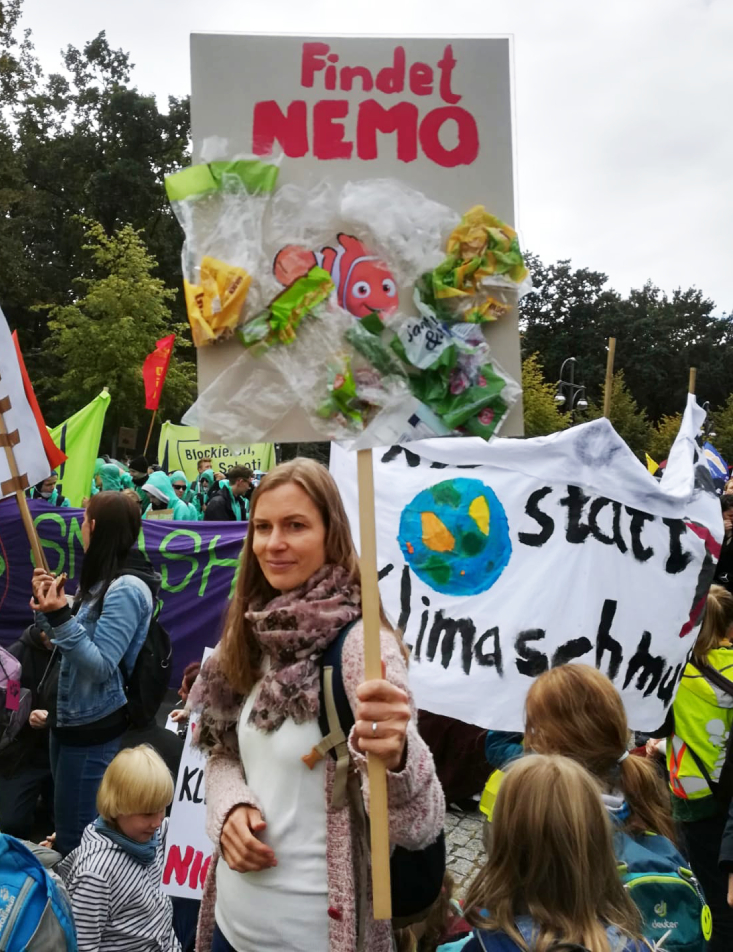 Foto: Frau in Menschenmenge hält Schild mit Fisch und aufgeklebten Plastik worauf Findet Nemo steht